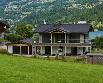 Modernes Haus mit Seeblick und Bergblick, umgeben von grüner Landschaft und einem Garten.