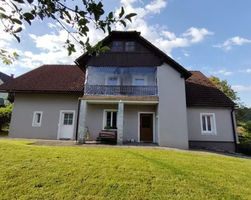 Vorderansicht des Hauses mit Balkon und gepflegtem Vorgarten unter blauem Himmel.