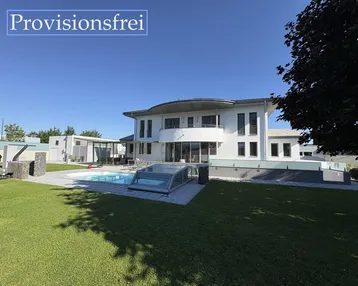 Moderne Villa mit großem Garten, Rasenfläche und einem überdachten Swimmingpool unter blauem Himmel.
