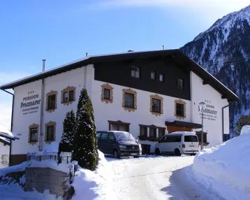 Die Pension Praxmarer präsentiert sich im Winter mit verschneiter Umgebung und geparkten Fahrzeugen vor dem Gebäude.