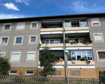 Fassade eines Mehrfamilienhauses mit mehreren Balkonen und Fenstern unter blauem Himmel.