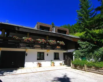 Traditionelles Haus mit Balkon, Blumenkästen und Blick auf die grüne Berglandschaft.