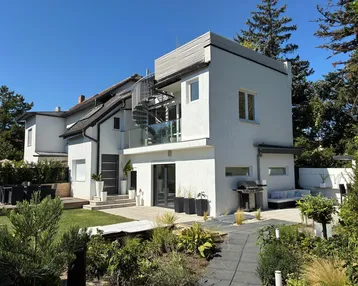 Modernes Haus mit weißer Fassade, gepflegtem Garten, Terrasse und Außentreppe zu einem Balkon.
