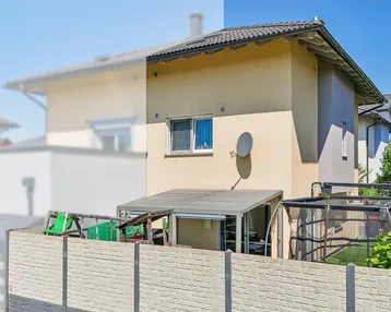 Außenansicht des Hauses mit überdachtem Sitzbereich und Trampolin im Garten.