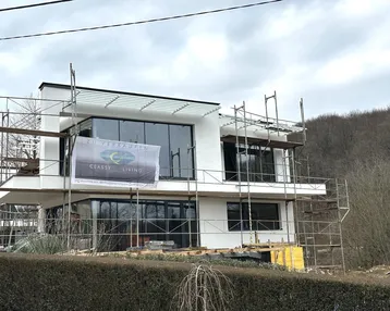 Modernes Neubauhaus im Bau mit Gerüst und einem "Zu Verkaufen"-Banner an der Fassade.