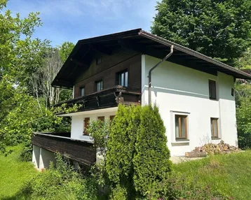 Traditionelles Haus mit weißer Fassade und dunklen Holzelementen, umgeben von üppigem Grün.