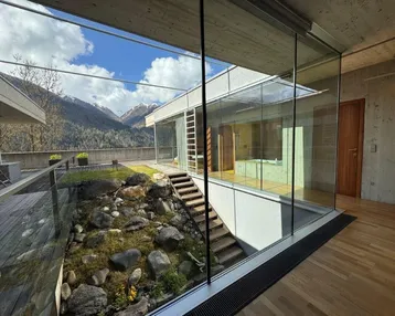 Moderner Innenbereich mit Holzboden, Glasfassade und Blick auf einen Felsengarten und die Berge.