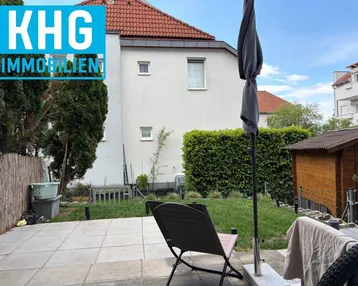 Gepflasterte Terrasse mit Gartenmöbeln, Rasenfläche und einem kleinen Gartenhaus im Außenbereich.