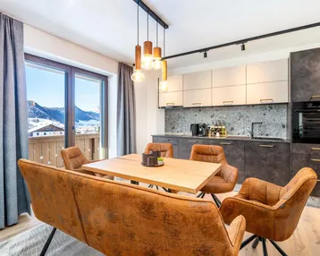 Moderner Wohn-Essbereich mit integrierter Küche, Holzboden und Balkonzugang mit Bergblick.
