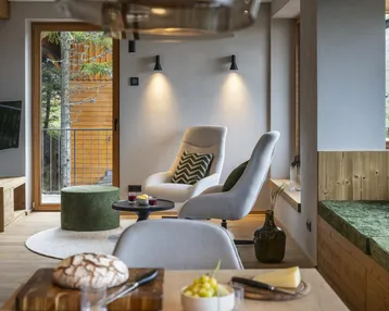 Gemütlicher Wohnbereich mit modernen Sesseln, Holzelementen und Zugang zum Balkon.