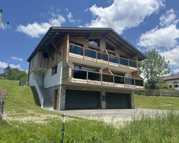 Modernes Holzhaus mit Steinfassade, Balkonen und integrierter Doppelgarage in alpiner Umgebung.