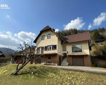 Traditionelles Einfamilienhaus mit Satteldach und Balkon in ländlicher Umgebung mit Bergblick.