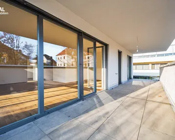 Große, sonnige Terrasse mit Fliesenboden und Blick auf die Umgebung, ideal für Entspannung im Freien.