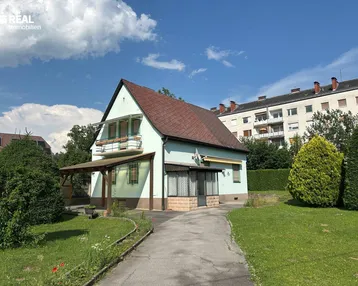 Charmantes Einfamilienhaus mit hellgrüner Fassade, braunem Dach und gepflegtem Vorgarten.