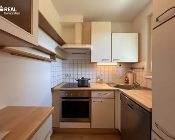 Funktionale Einbauküche mit hellen Schränken, Holz-Arbeitsplatten und modernen Geräten.