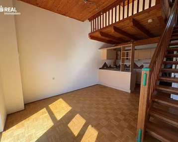 Heller Wohnbereich mit Holzdecke, Parkettboden und integrierter Küchenzeile unter einer Galerie.