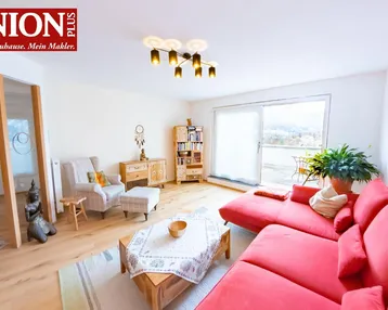 Helles Wohnzimmer mit rotem Sofa, Parkettboden und Zugang zu einem Balkon mit Bergblick.