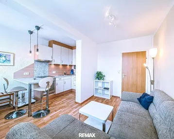 Helles Wohnzimmer mit offener Küche, Parkettboden und gemütlichem Sofa in einem kombinierten Bereich.