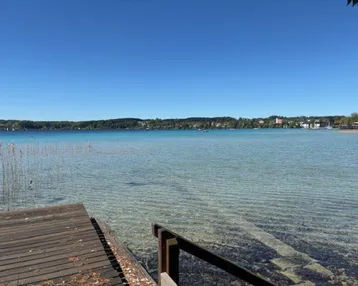 Klarer blauer See mit einem Holzsteg im Vordergrund unter strahlend blauem Himmel.