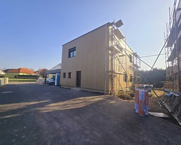 Neubau mit Holzfassade und Gerüst, noch im Bau befindlich an einem sonnigen Tag.