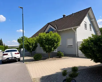Modernes Einfamilienhaus mit gepflegtem Vorgarten und gepflasterter Auffahrt unter blauem Himmel.