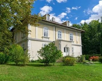 Klassische Villa mit heller Fassade und gepflegtem Vorgarten unter blauem Himmel.