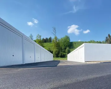Reihen von modernen Garagenboxen mit weiß gestrichenen Toren und asphaltierter Zufahrt in ländlicher Umgebung.