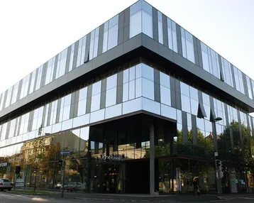 Modernes Bürogebäude mit Glasfassade und reflektierenden Fenstern an einer städtischen Straße.