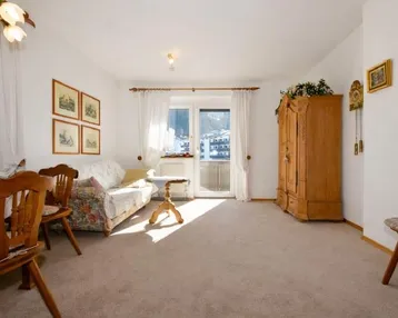 Helles Wohnzimmer mit gemütlichem Sofa, traditionellen Holzmöbeln und Zugang zu einem Balkon mit Bergblick.