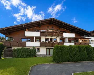 Traditionelles Alpenhaus mit Holzfassade, mehreren Balkonen und gepflegtem Vorgarten unter blauem Himmel.