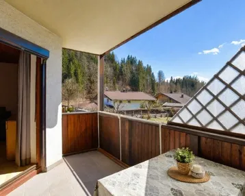 Balkon mit Holzelementen, Tisch und Stühlen, bietet einen weiten Blick auf die bewaldete Landschaft.