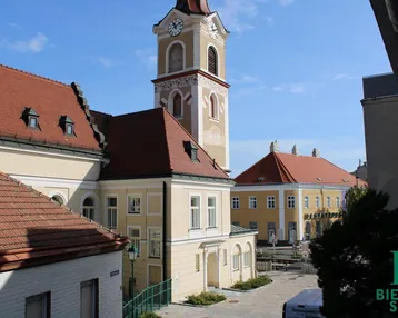 Blick auf eine historische Straße mit einer Kirche und traditionellen Gebäuden unter blauem Himmel.