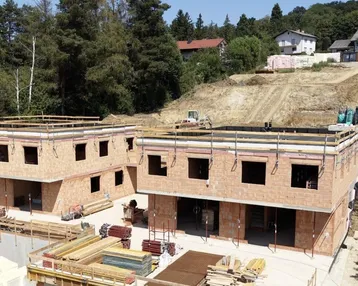 Baustelle mit mehreren im Bau befindlichen Reihenhäusern in hügeliger Landschaft.