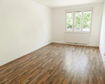 Helles, leeres Zimmer mit Laminatboden und Fensterblick ins Grüne, ideal als Wohn- oder Schlafzimmer.