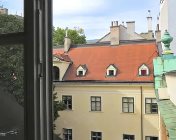 Blick aus dem Fenster auf die Dächer und Fassaden umliegender historischer Gebäude im Innenhof.