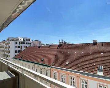 Blick vom Balkon über die Dächer der Stadt an einem sonnigen Tag mit blauem Himmel.