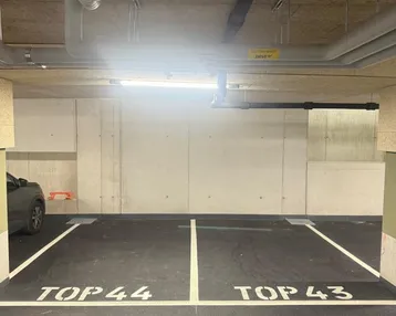 Tiefgarage mit markierten Stellplätzen und sichtbaren Installationen an der Decke.