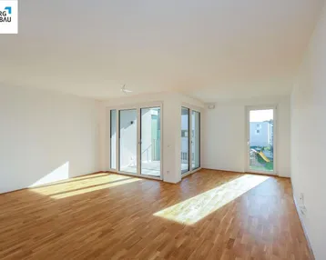 Helles Wohnzimmer mit Parkettboden und Zugang zu einem Außenbereich, durchflutet von natürlichem Licht.