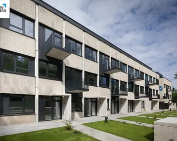 Moderne Wohnanlage mit mehreren Etagen, Balkonen und gepflegten Grünflächen unter blauem Himmel.