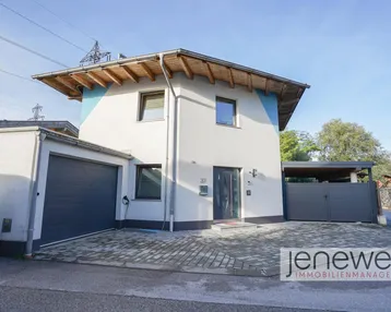 Modernes Einfamilienhaus mit Garage, Carport und gepflastertem Vorplatz unter blauem Himmel.
