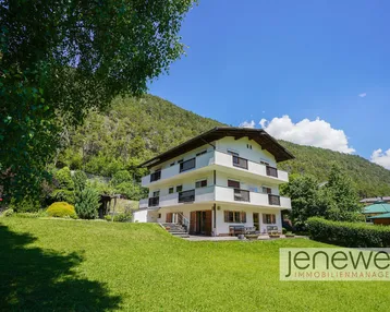 Großzügiges Anwesen mit Mehrfamilienhaus und weitläufigem Garten vor alpiner Bergkulisse.