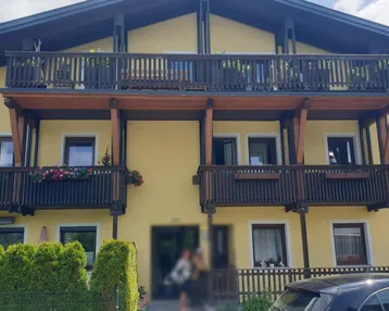Traditionelles Gebäude mit gelber Fassade und mehreren Holzbalkonen, geschmückt mit Blumenkästen.