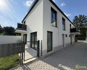 Moderne Neubaufassade mit klaren Linien, großen Fenstern und kleinen Balkonen unter blauem Himmel.