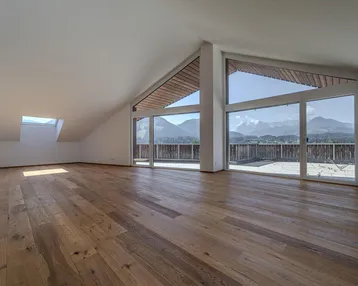 Geräumiger, lichtdurchfluteter Wohnbereich mit Holzboden, Dachschrägen und beeindruckendem Bergblick.