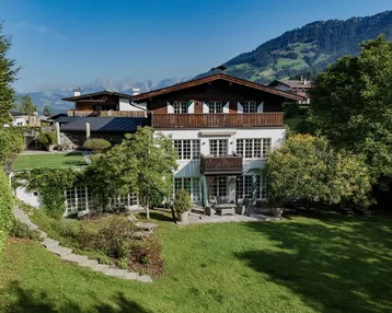Großzügiges Anwesen mit Bergblick, umgeben von einem gepflegten Garten und Bäumen.