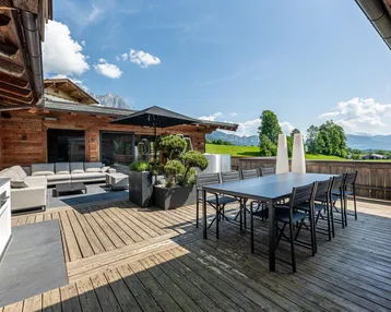 Geräumige Holzterrasse mit Essbereich, Lounge-Möbeln und weitem Blick auf die Landschaft und Berge.