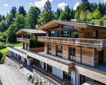 Luxuriöses Holzchalet mit mehreren Balkonen und Terrassen, eingebettet in eine grüne Berglandschaft.