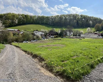 Weitläufiges Grundstück mit Schotterweg und Blick auf die umliegende grüne Landschaft und Häuser.