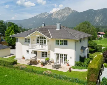Elegantes Haus mit großer Terrasse und Garten, umgeben von einer malerischen Berglandschaft.