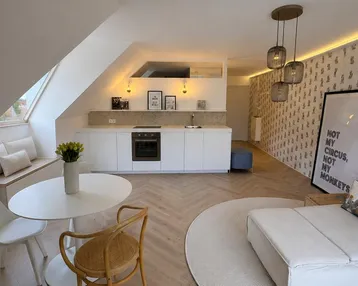 Helles, offenes Dachgeschoss-Apartment mit integrierter Küche, Essbereich und gemütlicher Sitzecke unter der Dachschräge.